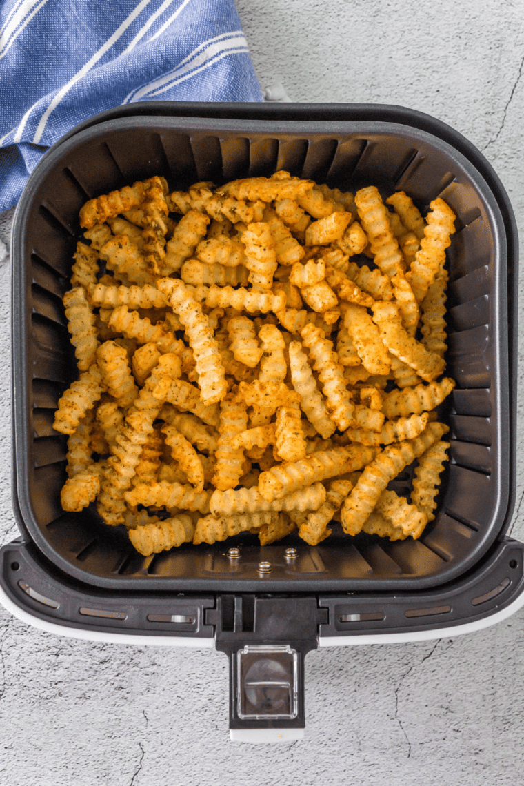 Crinkle cut fries cooking in an air fryer basket, shaking halfway through for crispy golden edges.