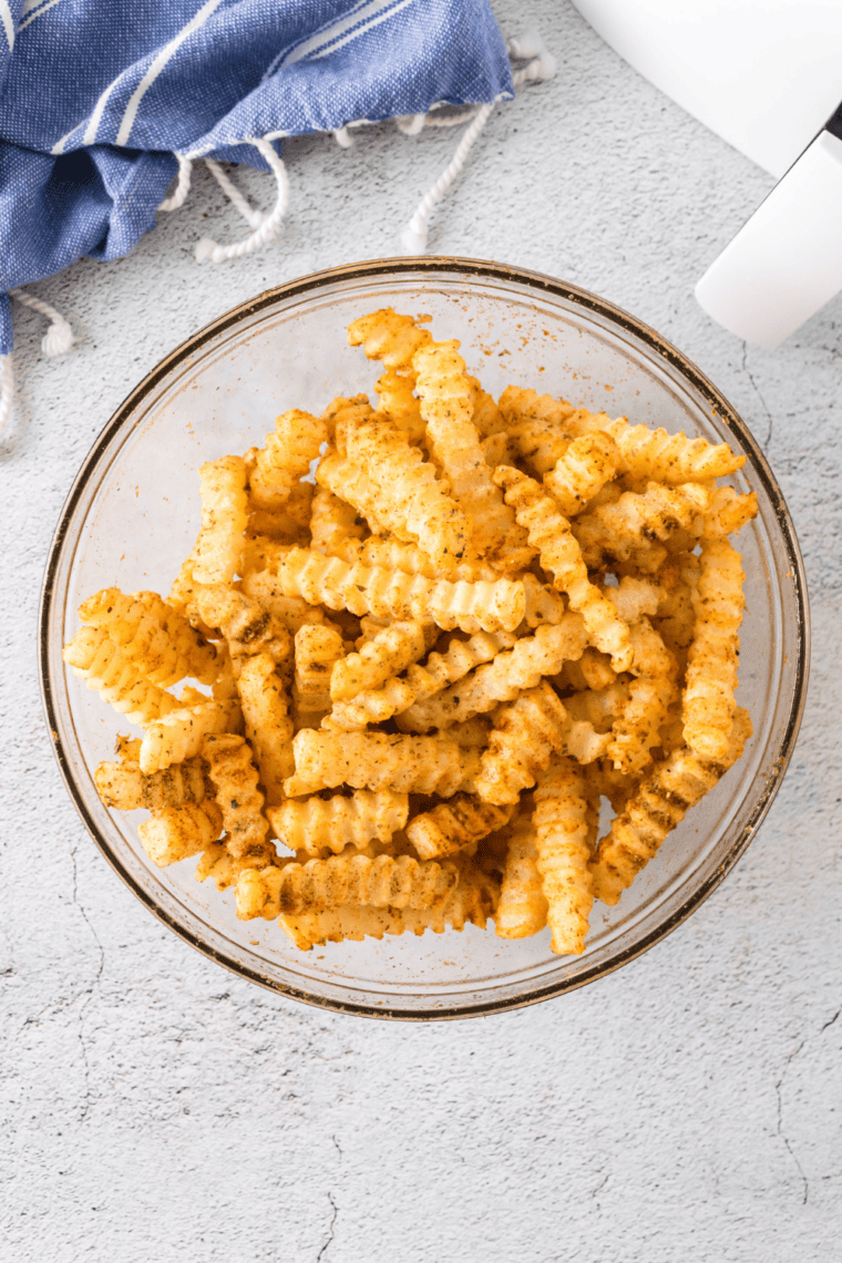 Crinkle fries being tossed in oil and seasonings in a bowl until evenly coated.