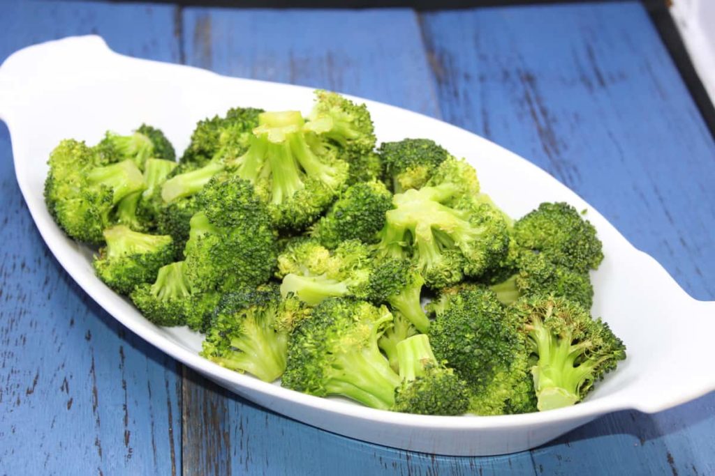 roasted broccoli in white dish on blue wooden surface