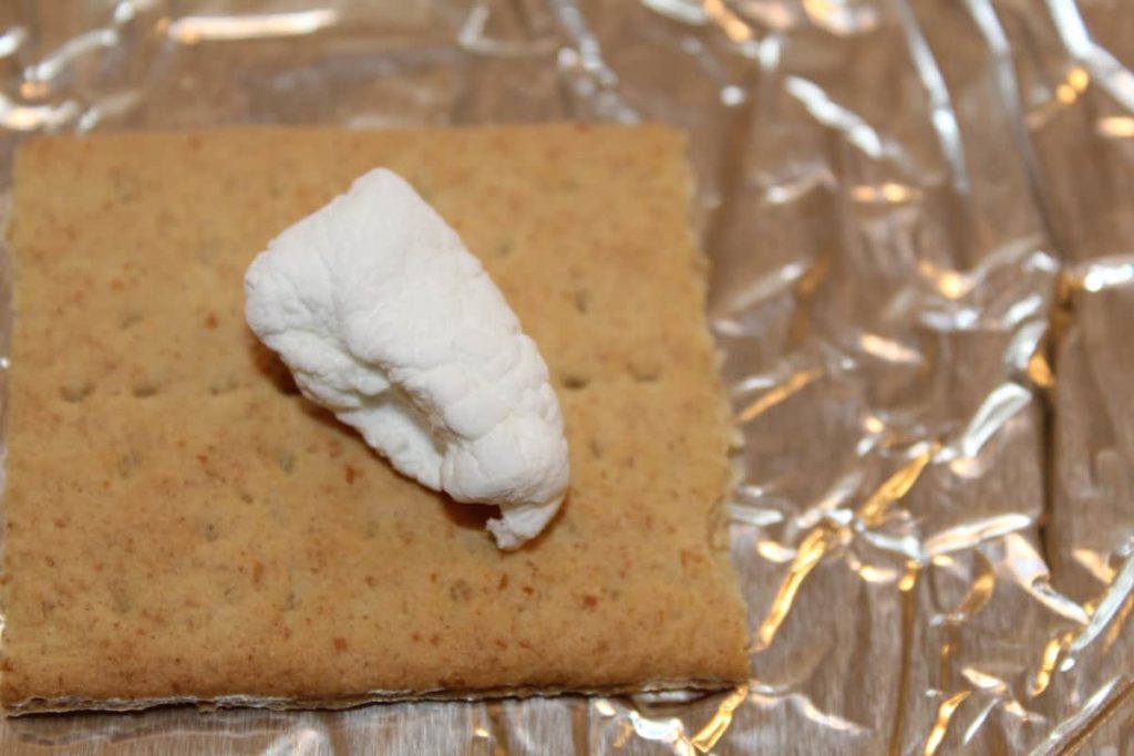 graham cracker topped with half a jumbo marshmallow on foil