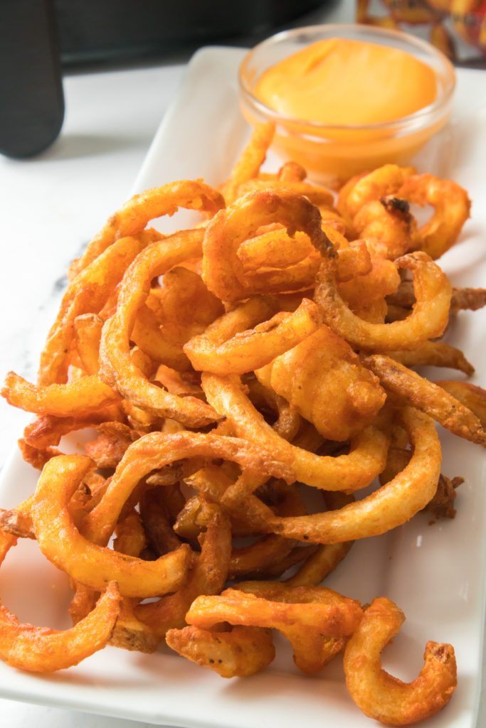 overhead of air fryer curly fries on a rectangle plate with dipping sauce