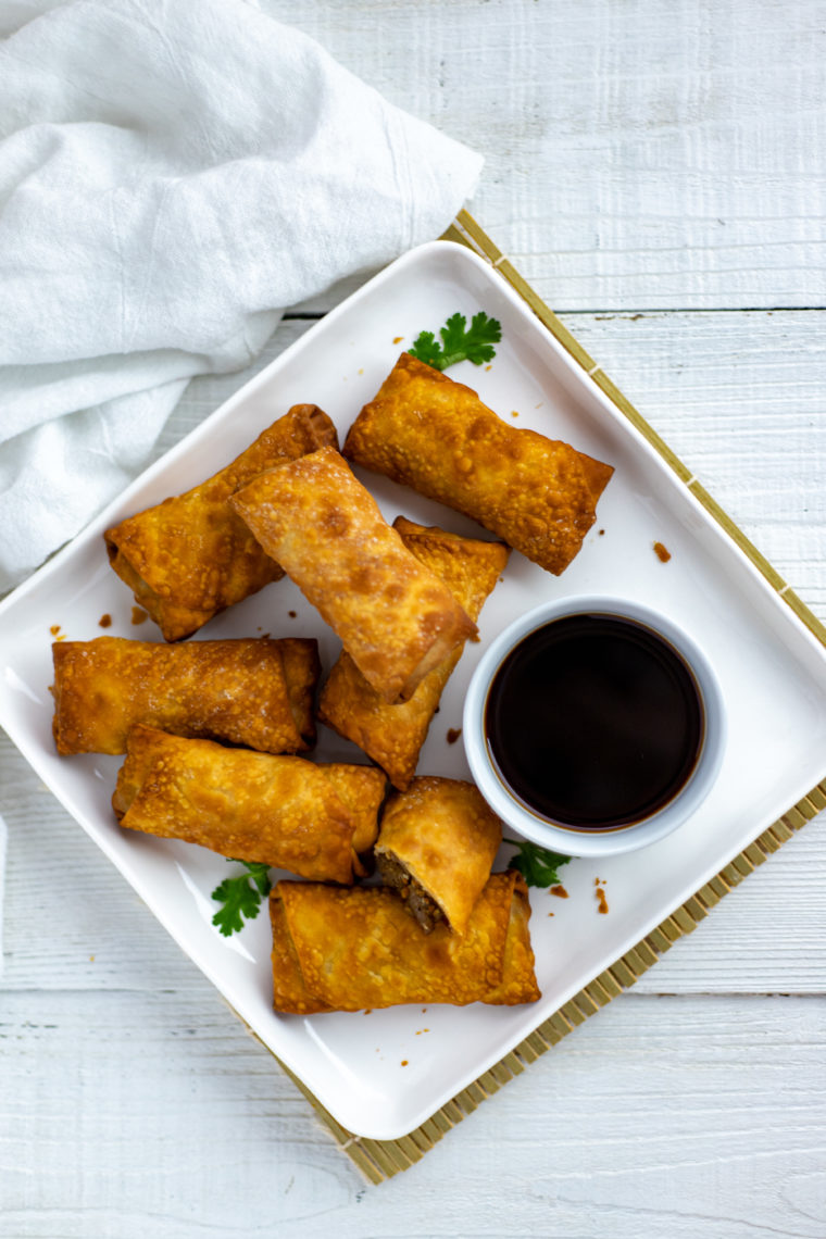 overhead: air fryer lumpia on a white plate with a small bowl of dipping sauce