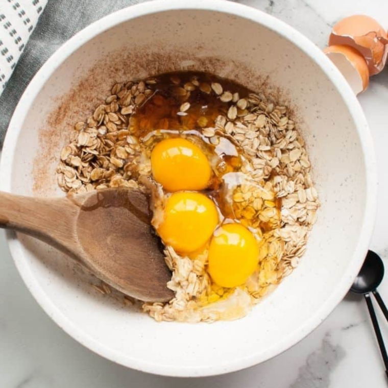 Cherry oatmeal ingredients in bowl with eggs and wooden spoon