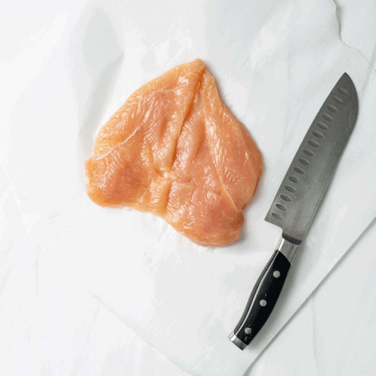 Butterflying a chicken breast with a sharp knife, leaving a hinge for stuffing.