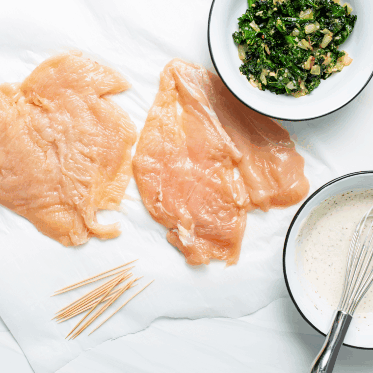 Seasoned chicken breast being stuffed with feta cheese and spinach before folding.
