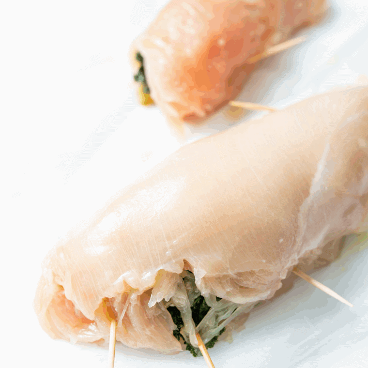 Chicken breast coated with egg wash and bread crumbs, ready in air fryer basket with toothpicks securing the seam.