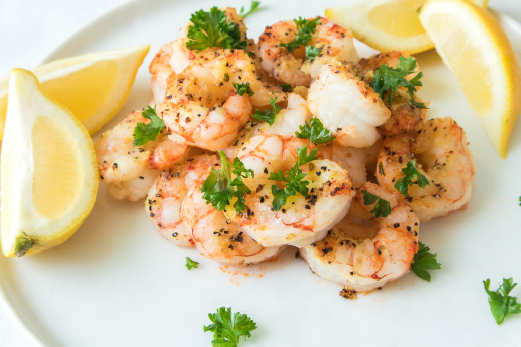 close up of cooked shrimp with fresh parsley and lemon wedges