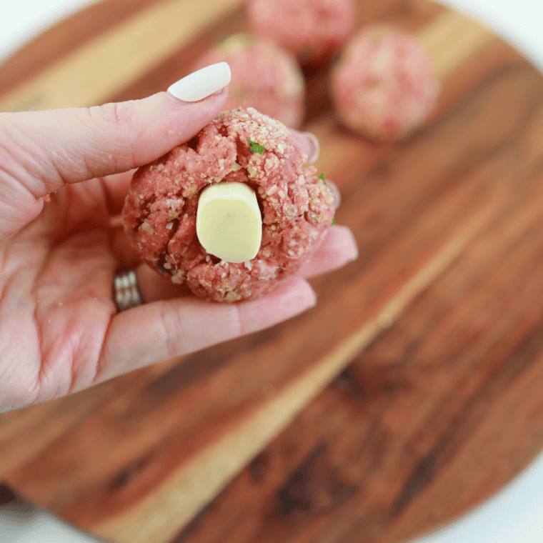 Pressing a mozzarella cube into the center of each meatball.