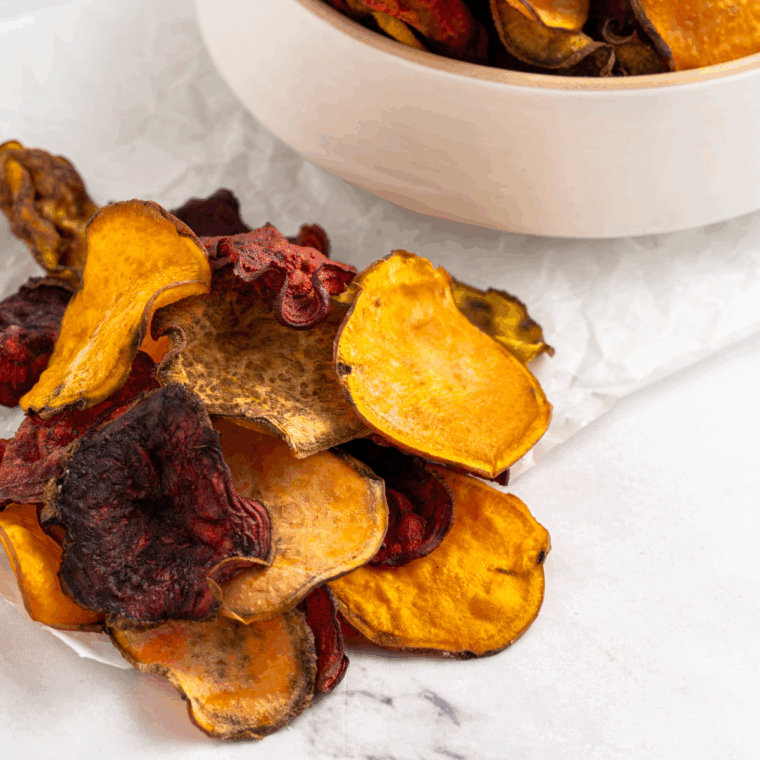 A bunch of vegetable root chips on parchment paper.