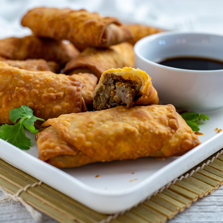 closeup side view: several lumpia on a white plate with one with a bit taken out of it so the filling is showing