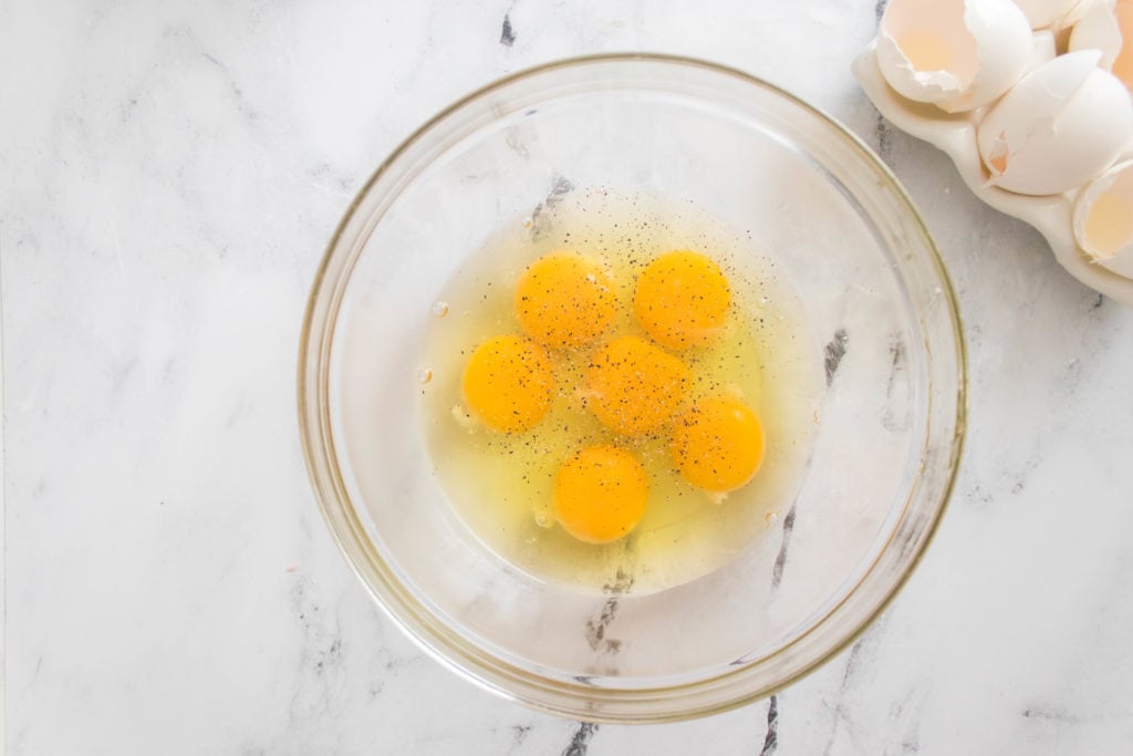 six cracked eggs with salt and pepper in a glass bowl
