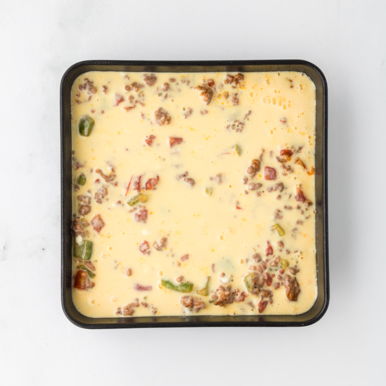 Mixing eggs, sour cream, and heavy cream in a bowl, preparing to pour over ground beef in air fryer dish.