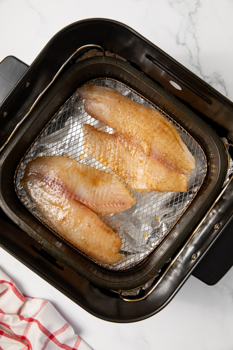 Walleye fillets arranged in a single layer in an air fryer basket cooking until golden, opaque, and flaky