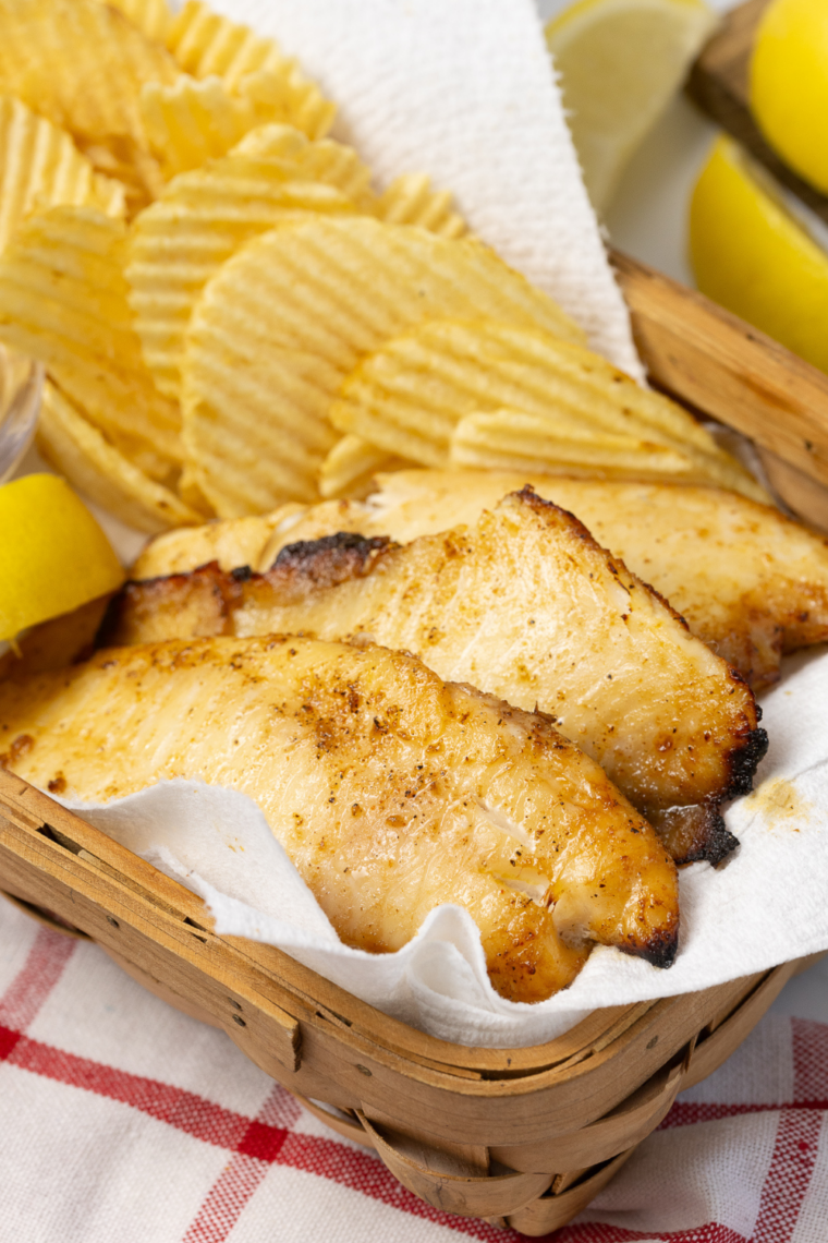 Flaky air fryer walleye fillets with no breading served on a plate with lemon wedges and fresh herbs