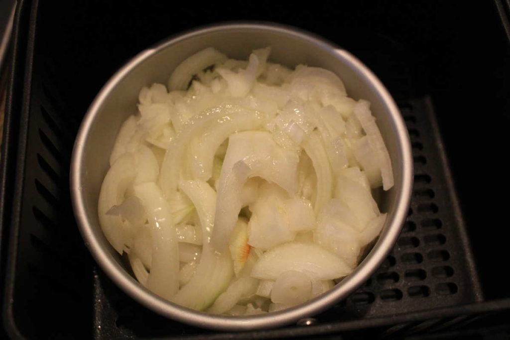 sliced onions in a metal pan in air fryer basket