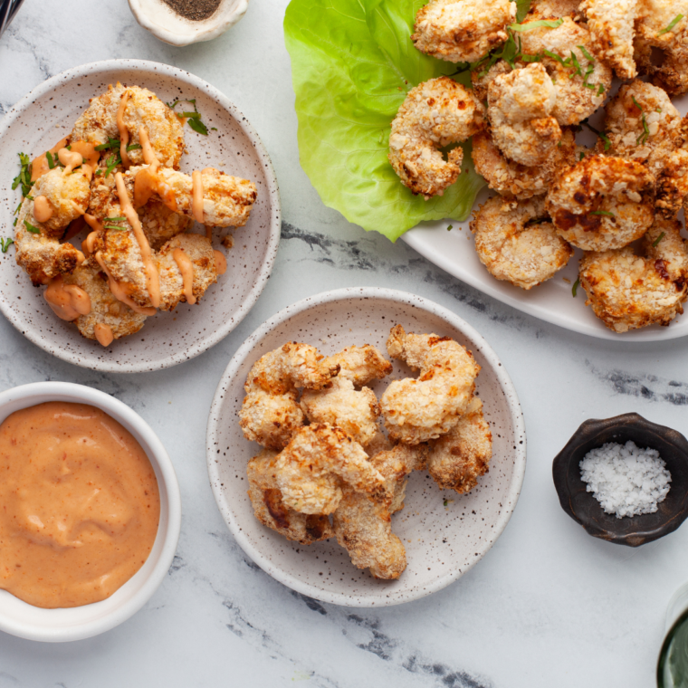 Coated shrimp arranged in a single layer in the air fryer basket, cooking to golden crispiness.