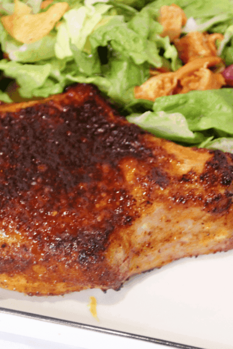 Air fryer chile lime pork chop cooked golden brown, garnished with lime wedges and fresh herbs.