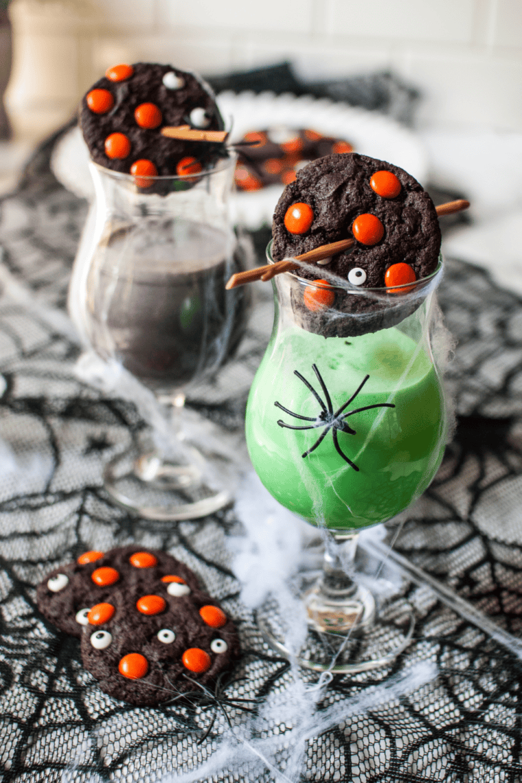 A batch of thick, dark chocolate cookies topped with vibrant orange M&M's and spooky white candy eyeballs, cooling on a wire rack to show their soft, fudgy texture.