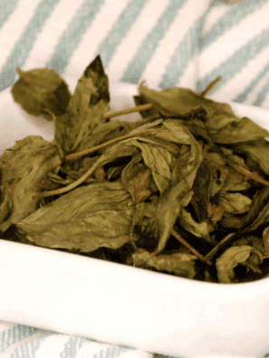 Dried basil leaves in a small bowl with fresh basil and an air fryer in the background.
