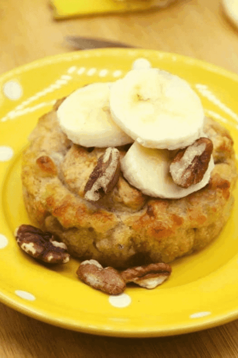 A small ceramic mug containing banana bread batter being placed into a compact air fryer basket.