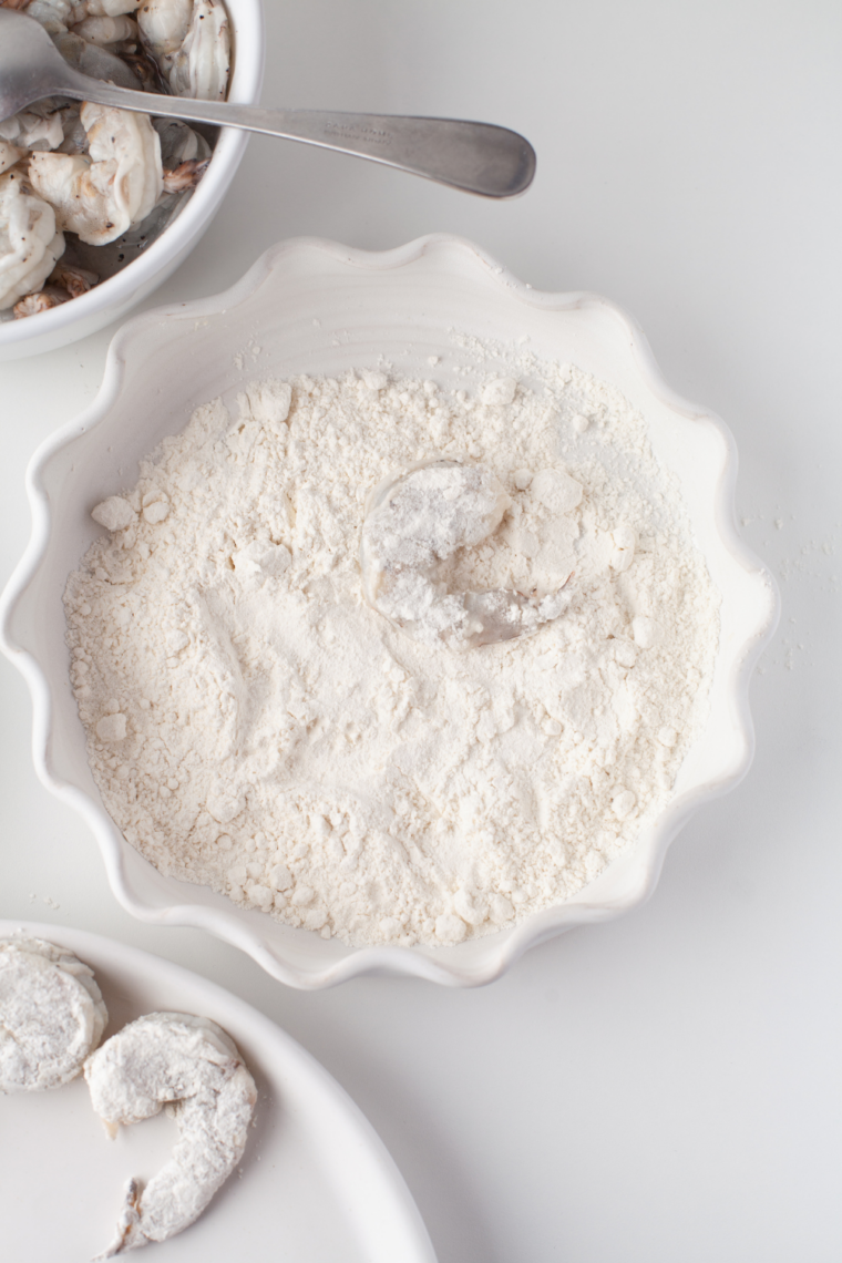 Bowl with flour, breadcrumbs, paprika, garlic powder, salt, and black pepper being mixed for shrimp coating.