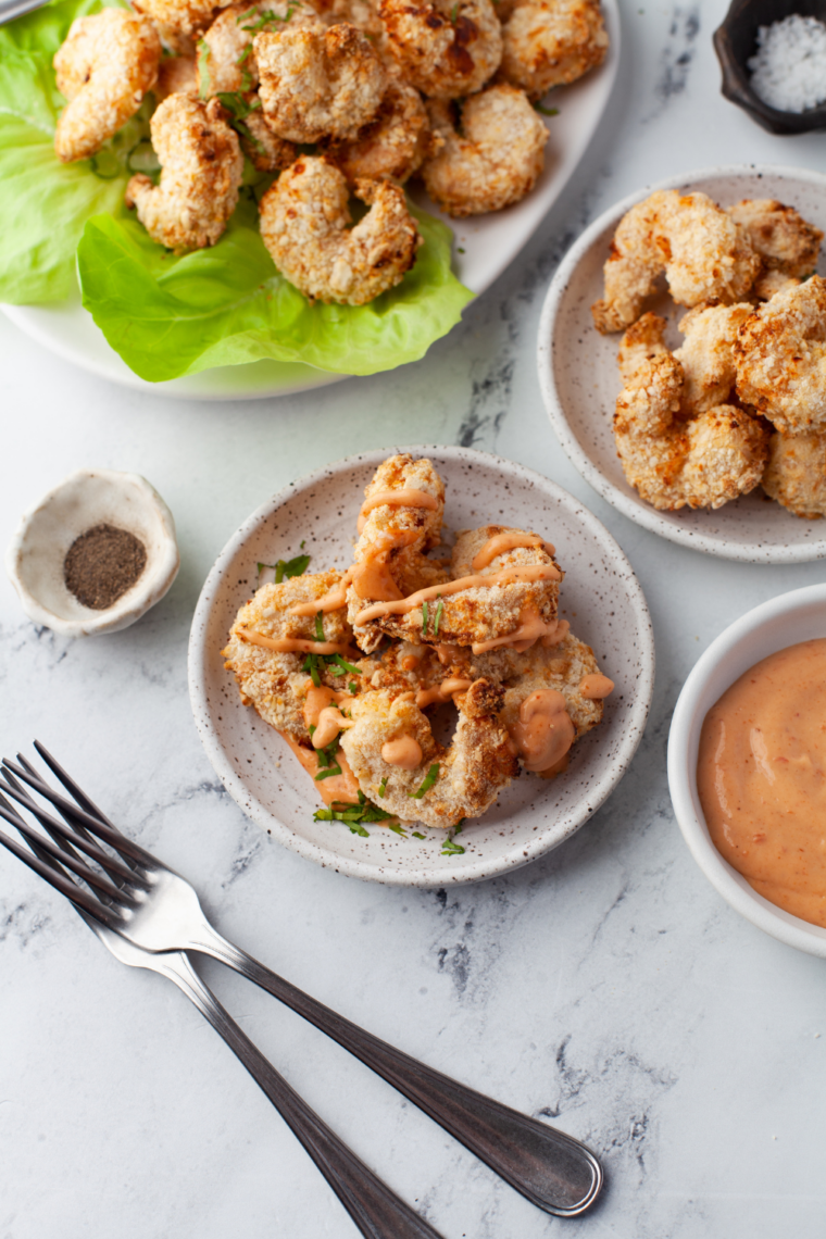 Golden crispy butterfly shrimp cooked in the air fryer served on a plate with dipping sauce and garnished with herbs