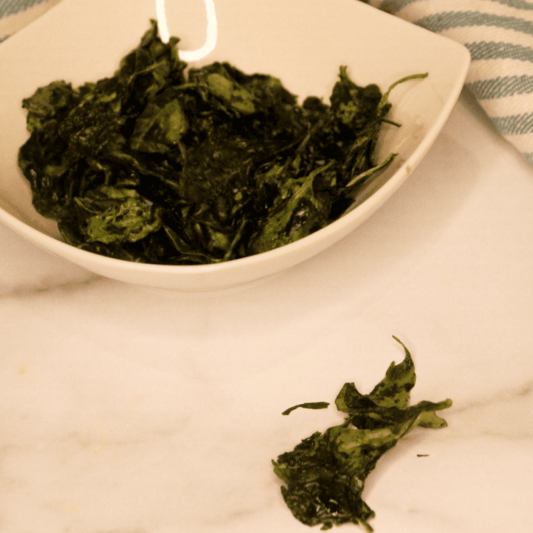Crispy air fryer spinach chips cooling on a plate after cooking.