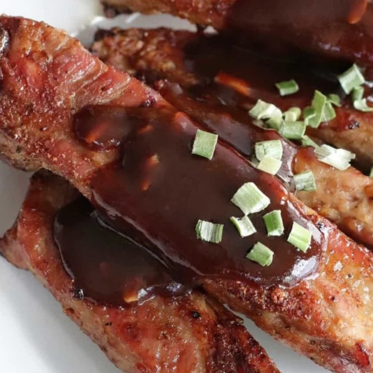 A plate of Air Fryer Fireball Glazed Ribs, golden brown with a sticky, caramelized glaze, garnished with fresh herbs