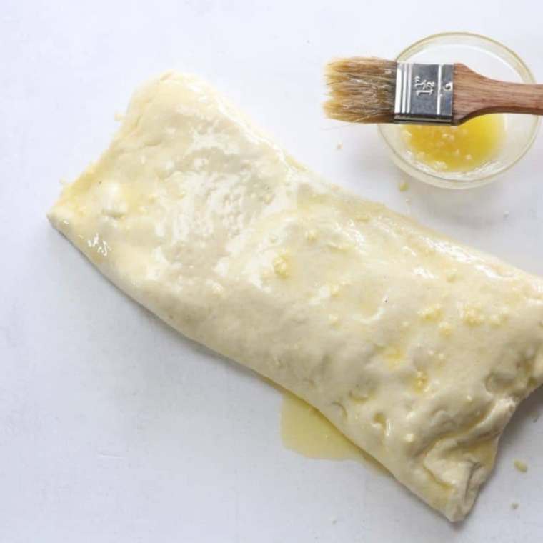 Coating rolled dough with melted butter and garlic.