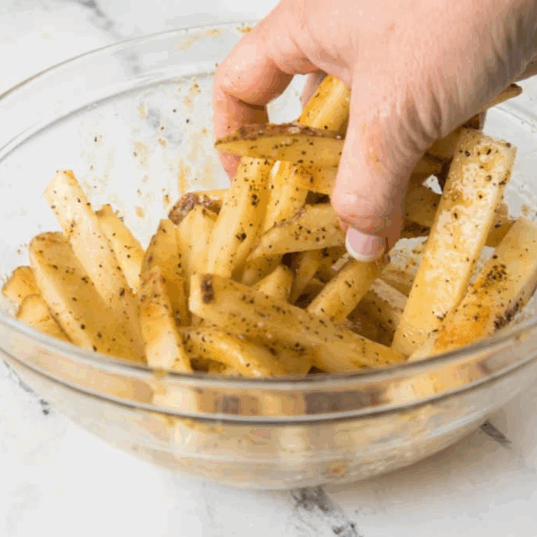 Cut russet potatoes tossed in olive oil, salt, and black pepper in a large bowl, evenly coated and ready for cooking.