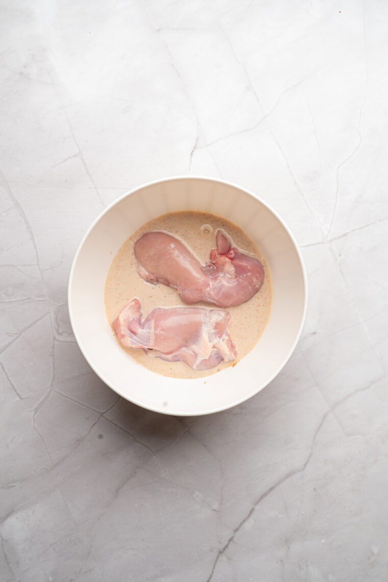 Chicken marinating in buttermilk with salt, pepper, and garlic powder in a bowl.