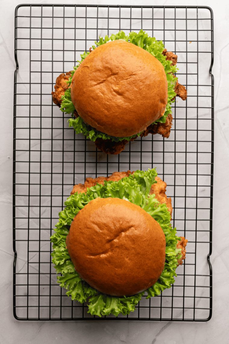 Crispy Copycat Wingstop Chicken Sandwich with golden fried chicken, lettuce, tomato, pickles, and sauce on a toasted bun, served on a plate.