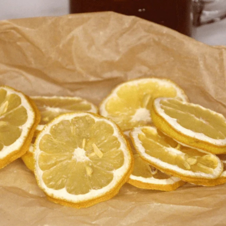 Partially dried lemon slices showing a leathery texture and deeper yellow color while finishing in the air fryer.