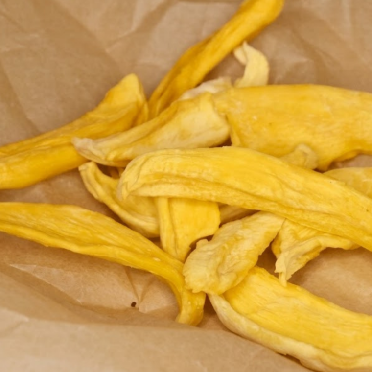 Sliced mango pieces laid in a single layer inside an air fryer basket, slowly dehydrating into chewy, golden dried fruit.