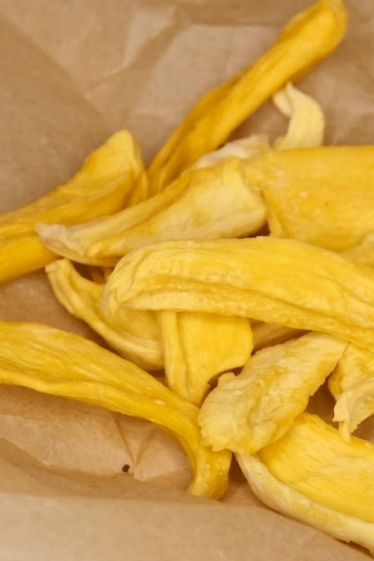 Sliced mango pieces arranged in a single layer in an air fryer basket, slowly dehydrating into chewy, golden dried fruit.