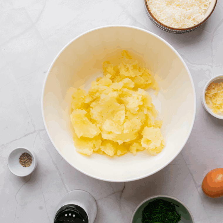 Mixing mashed potatoes, cheddar, sour cream, seasonings, half the bacon, and half the green onions in a large bowl