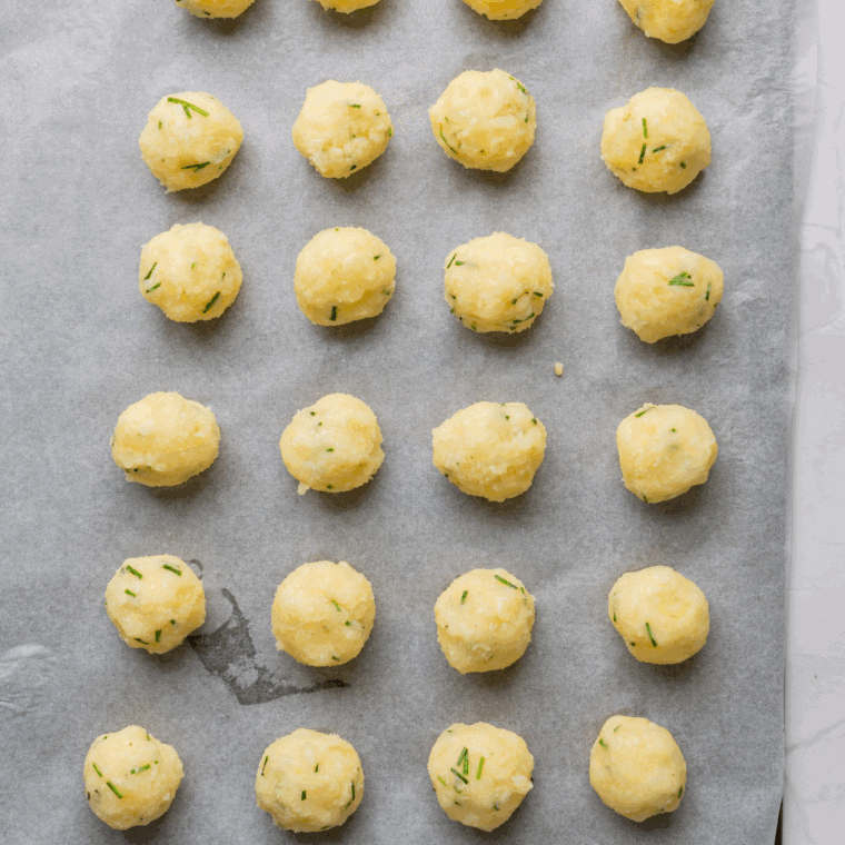 Shaping potato mixture into small, bite-sized tots on a greased baking sheet
