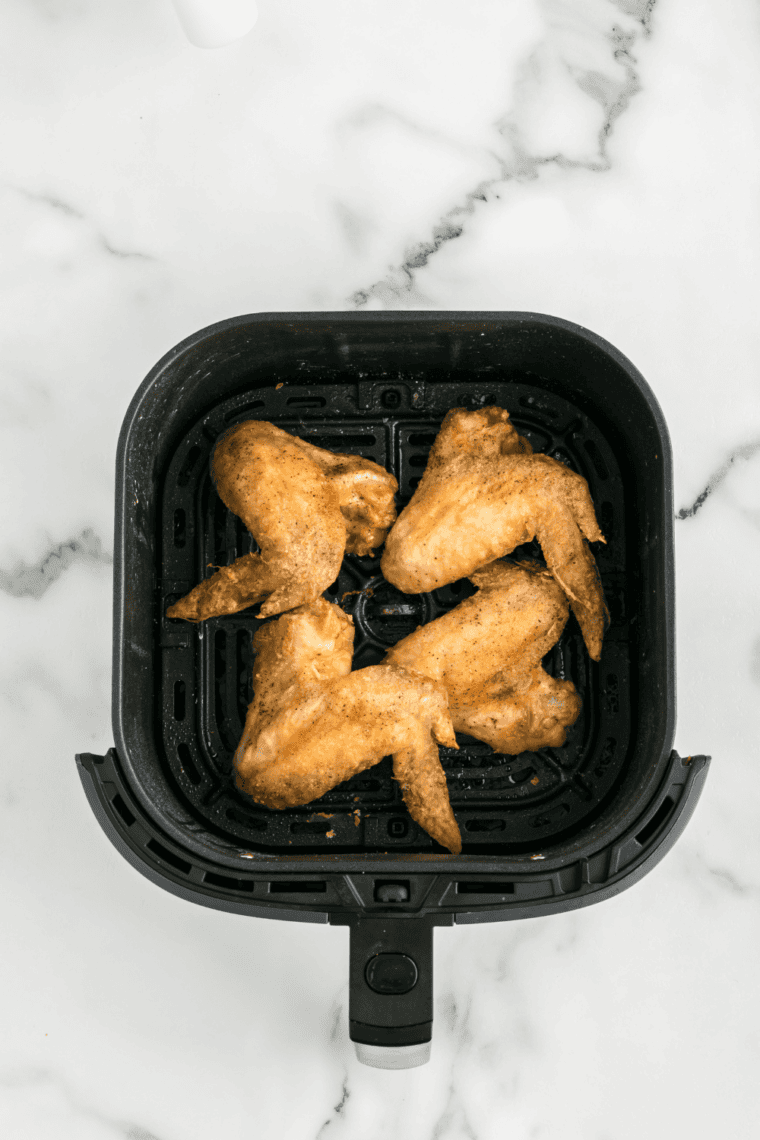 Cooked chicken wings in the air fryer basket.