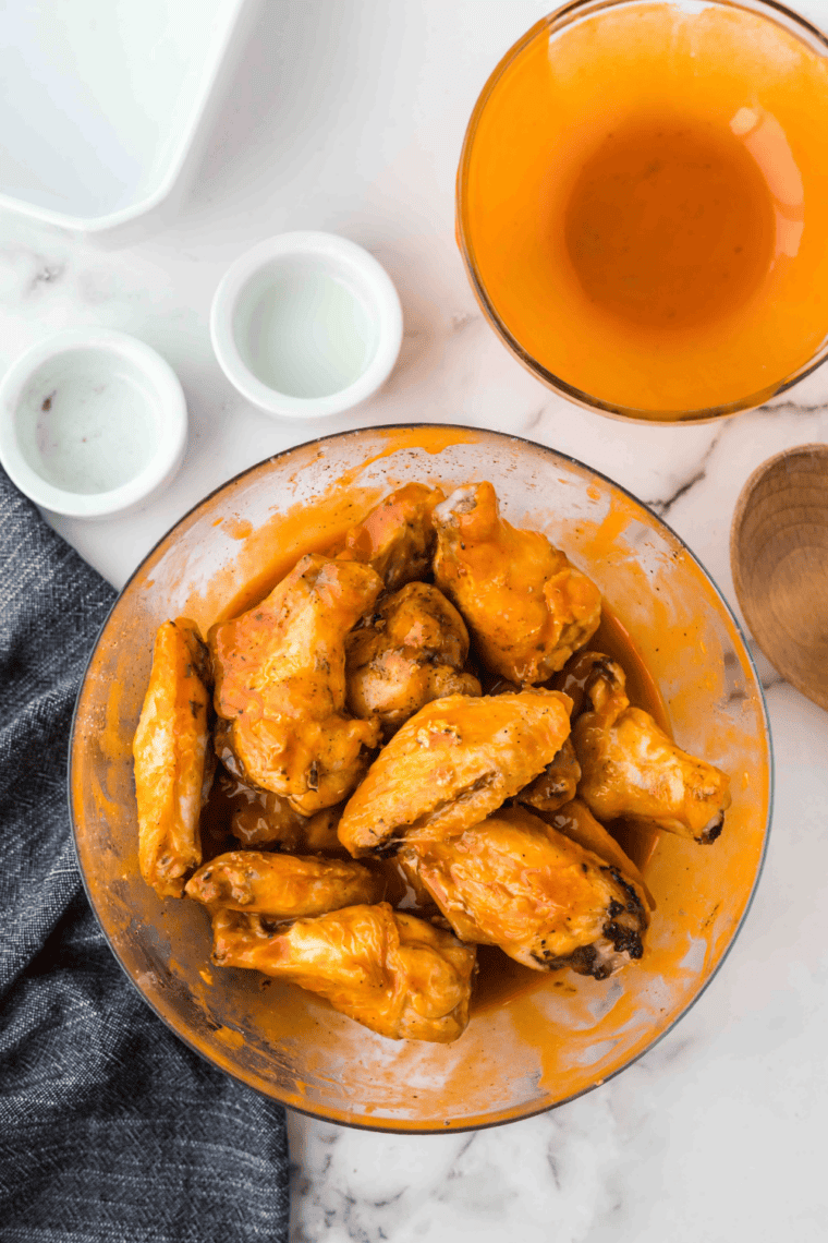 Tossing crispy cooked wings in homemade spicy buffalo sauce until fully coated.