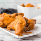 Crispy golden chicken wings coated in spicy buffalo sauce, served on a plate with dipping sauce.