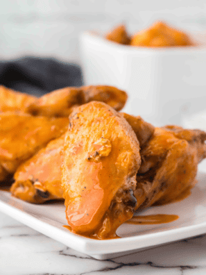 Crispy golden chicken wings coated in spicy buffalo sauce, served on a plate with dipping sauce.