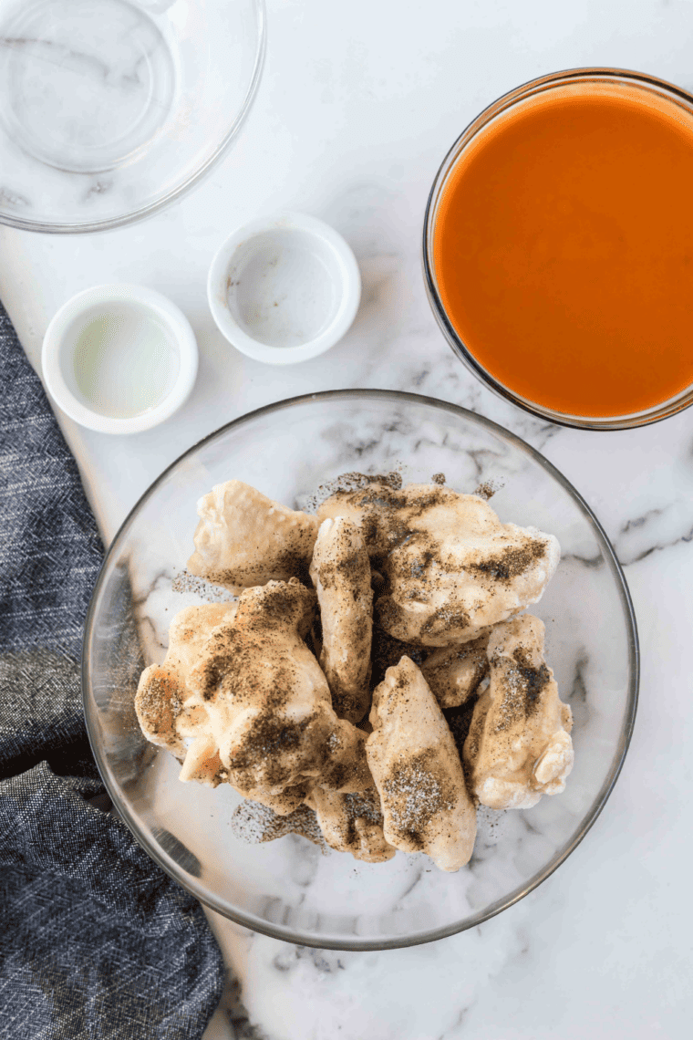 Seasoning chicken wings in a large bowl with salt, pepper, garlic powder, paprika, cayenne, and onion powder.