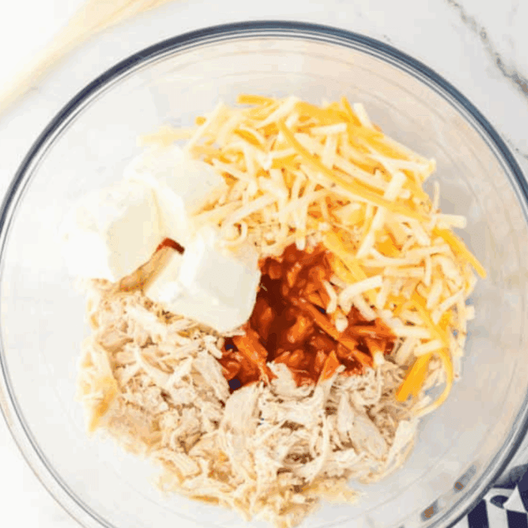 A large mixing bowl filled with shredded chicken, cream cheese, shredded cheddar, and hot sauce, ready to be mixed for buffalo chicken wontons.
