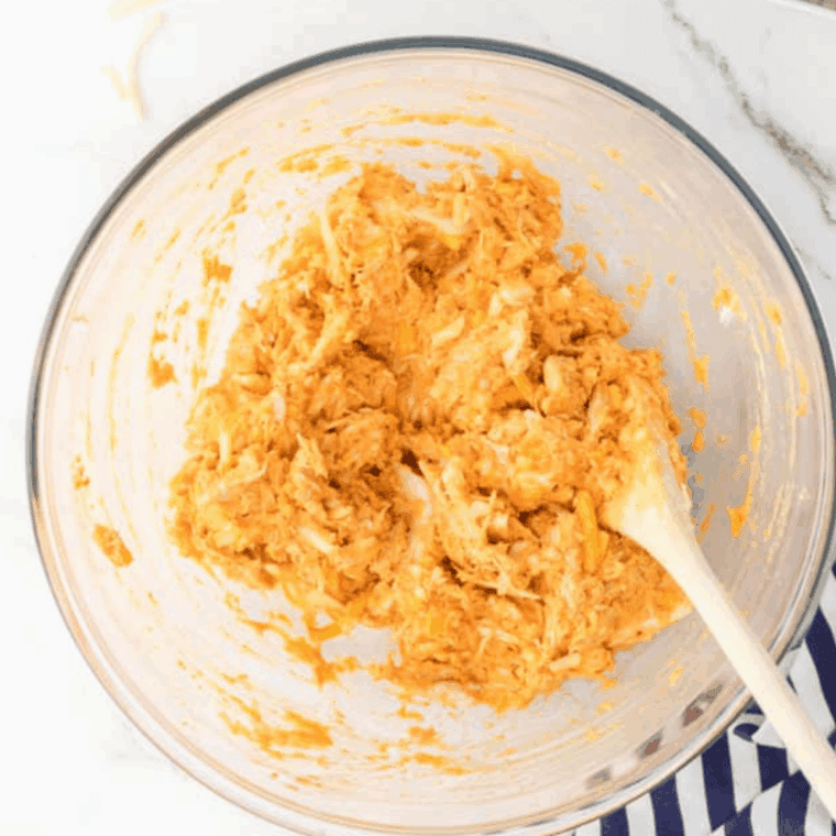Buffalo chicken mixture in a bowl, fully mixed with cream cheese, cheddar, and hot sauce until evenly coated.