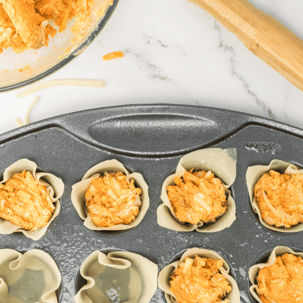 Wonton wrappers pressed into a muffin tin sprayed with oil, placed in the air fryer basket cooking at 400°F for 4–5 minutes until lightly crispy.