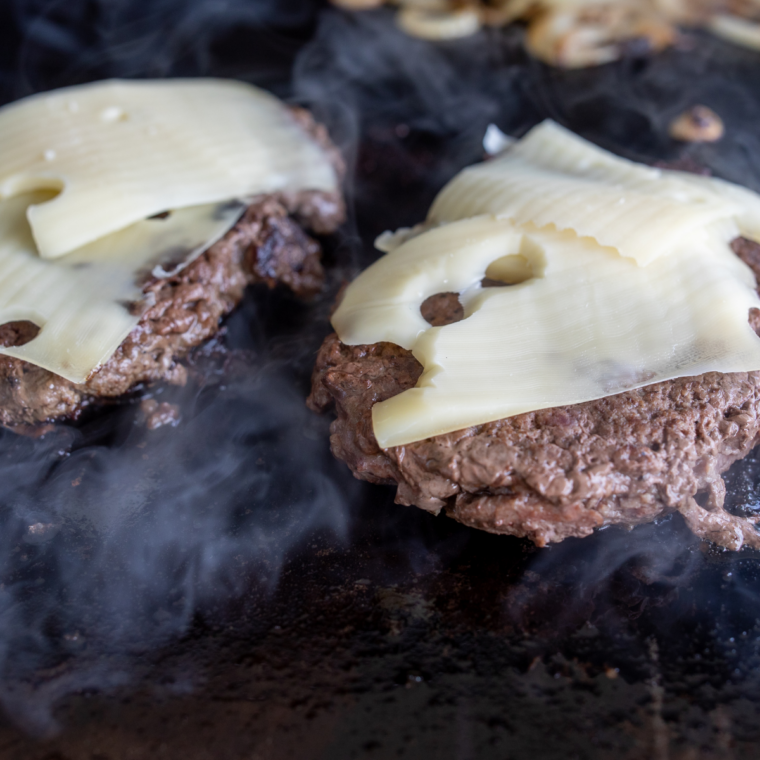 Frozen burgers cooking under basting dome on Blackstone griddle to keep patties juicy