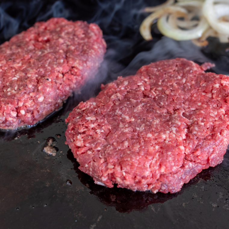 Frozen hamburger patties placed on hot Blackstone griddle with space between each burger