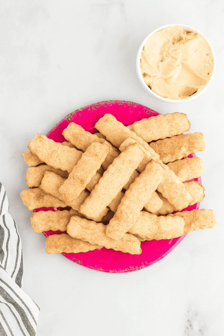Plate of golden, crispy Snickerdoodle Cookie Fries with a small bowl of cinnamon cream cheese dip