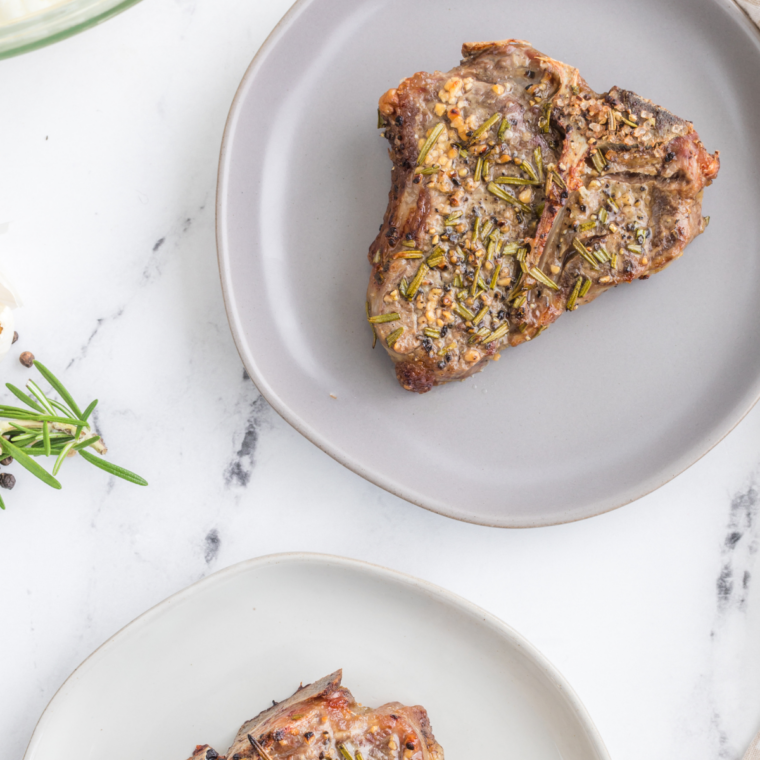 Cooked lamb chops resting on a white plate, seared golden-brown outside with a juicy pink center