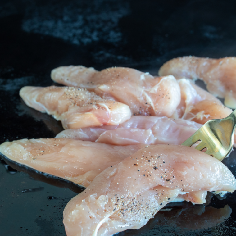Seasoned chicken cubes searing and charring on a hot oiled Blackstone griddle.